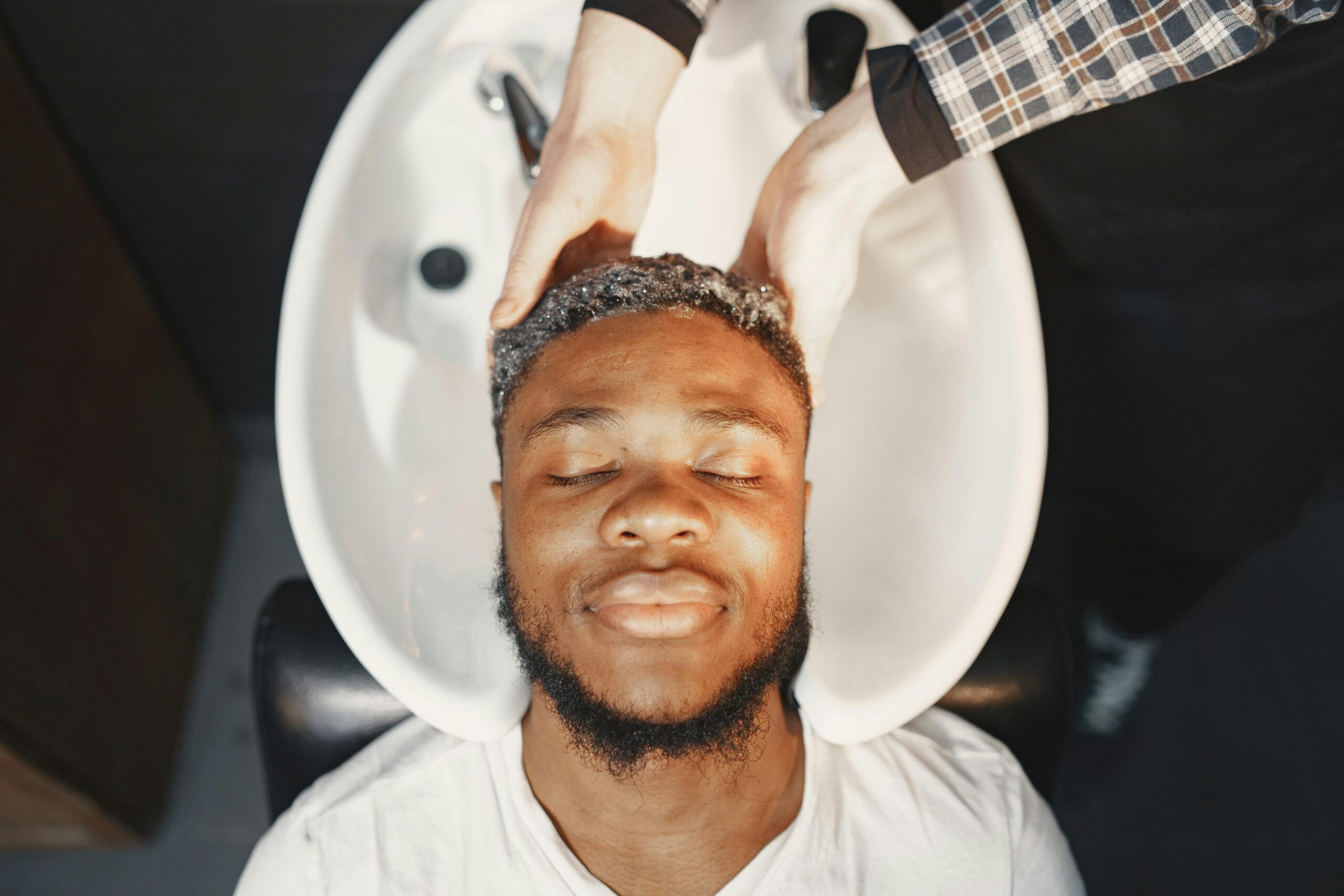 pexels photo 7447130 7447130 Man enjoying a relaxing hair wash at the barber shop, eyes closed and serene.