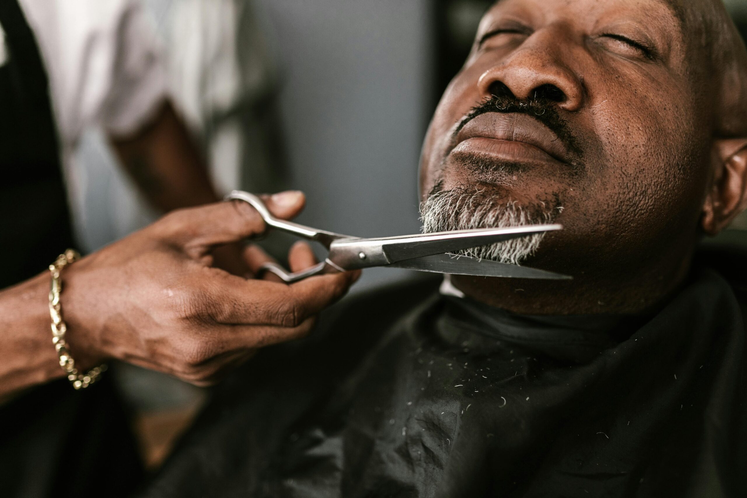 pexels photo 7697315 7697315 A professional barber skillfully trims a mature man's beard in a barbershop setting.